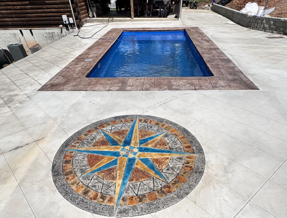 Hand-coloured compass rose medallion stamped into a concrete pool deck in blue, gold and rust tones &mdash; The Foothills Concrete Company
