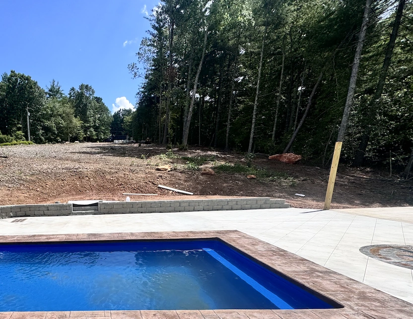 Concrete pool deck with a segmental block retaining wall holding a freshly graded slope at a wooded NC Foothills property &mdash; The Foothills Concrete Company